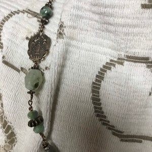 May include: A green and brown beaded necklace with a silver pendant featuring a floral design.