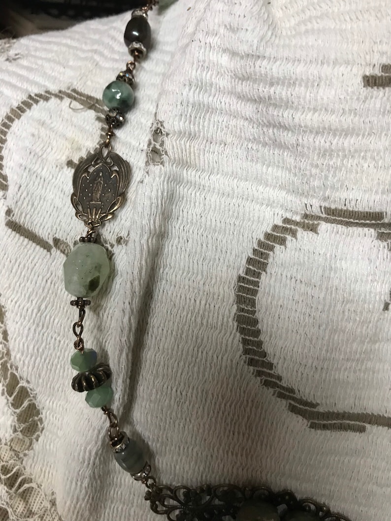 May include: A green and brown beaded necklace with a silver pendant featuring a floral design.