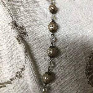 May include: A long necklace with alternating ivory-colored beads and clear crystal beads. The beads are connected by a silver chain.