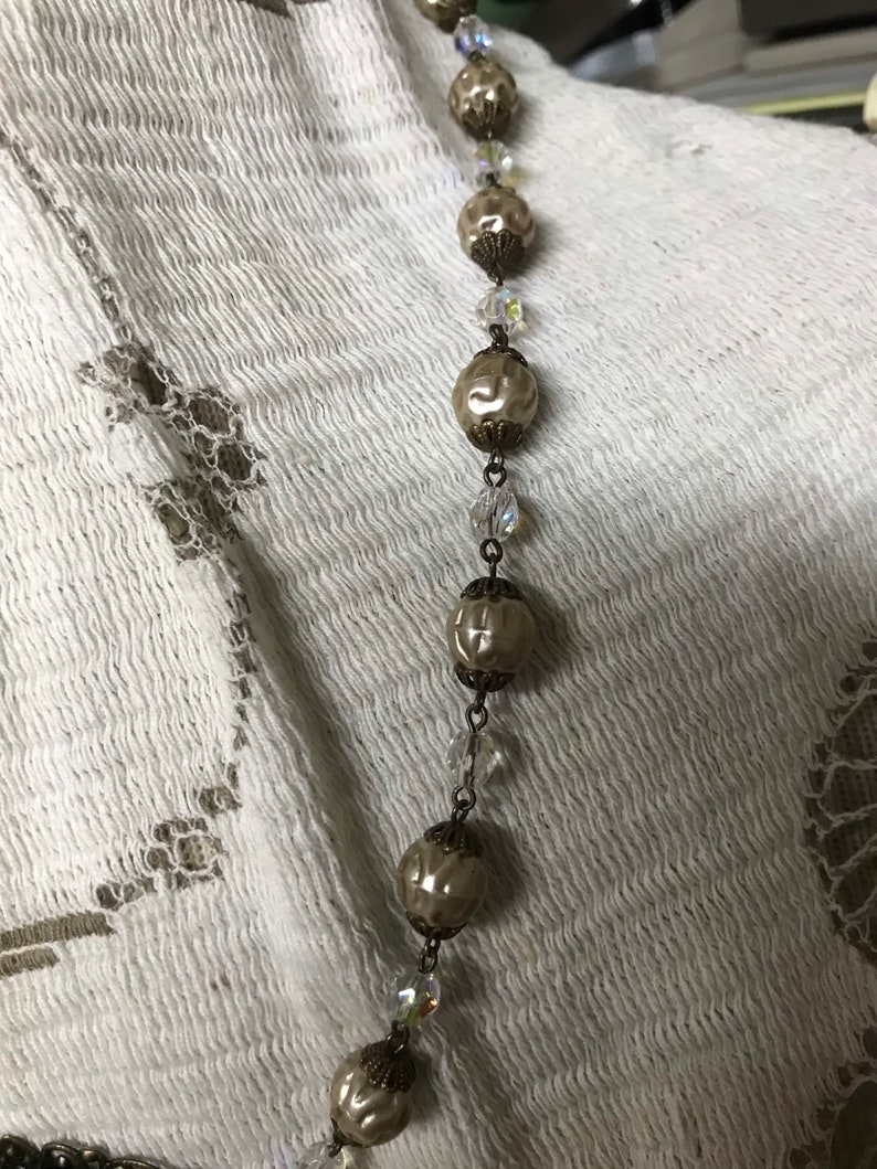 May include: A long necklace with alternating ivory-colored beads and clear crystal beads. The beads are connected by a silver chain.