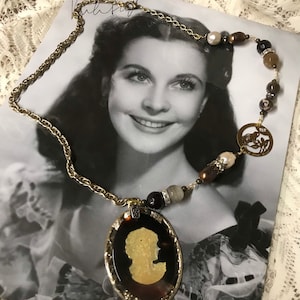 May include: A gold chain necklace with a cameo pendant featuring a woman's profile. The necklace is adorned with brown, black, and white beads.
