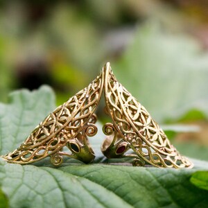 May include: Two gold filigree rings with red and green gemstones. The rings are designed in a leaf pattern and are set on a green leaf.