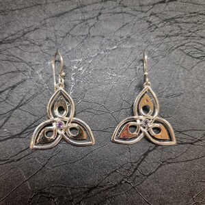 May include: A pair of silver earrings with a Celtic knot design and a small purple gemstone in the center of each earring.