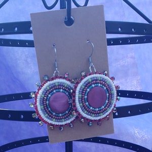 以下が含まれることがあります： ピンクの中心と白、赤、緑、紫のビーズが付いたビーズのイヤリングのペア