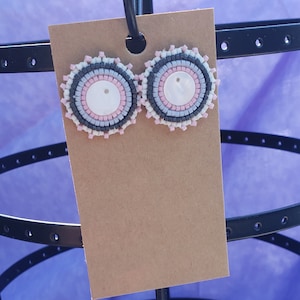 May include: A pair of round beaded earrings with a white center and layers of pink, gray, and black beads.