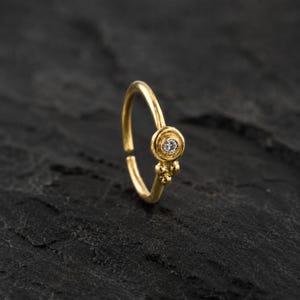 A gold nose ring with a small diamond in the center is displayed against a dark background.