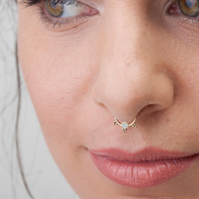A close-up of a woman's face, focusing on her nose and lips. She is wearing a gold nose ring with a small gemstone.