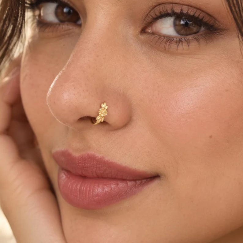 A close-up of a woman's face, focusing on her nose and lips. She is wearing a gold nose ring with a floral design.