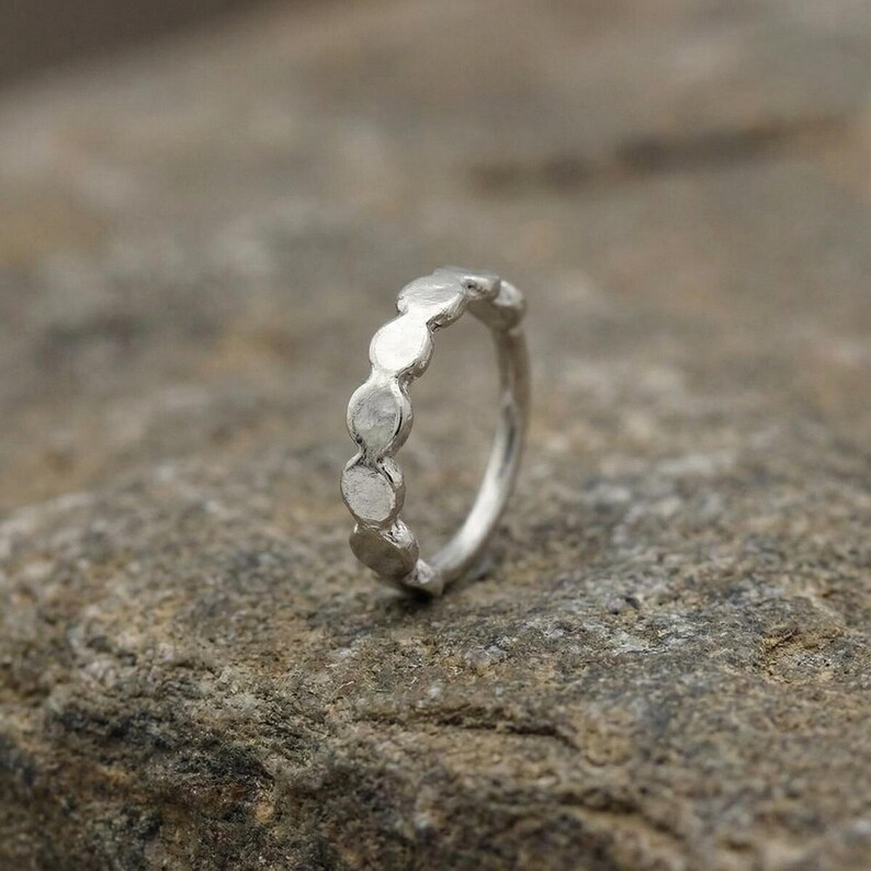 A silver ring with a unique design sits on a rock surface.