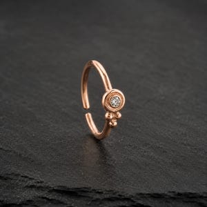A single, ornate gold-colored nose ring with a small diamond in the center, resting on a dark surface.