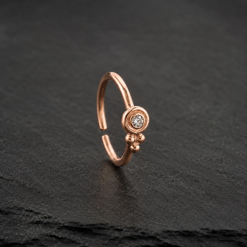 A single, ornate gold-colored nose ring with a small diamond in the center, resting on a dark surface.