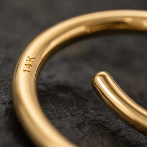 A close-up view of a gold bracelet or bangle with the text "14K" engraved on it, resting on a dark surface.