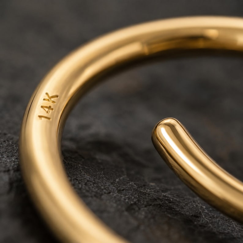 A close-up view of a gold bracelet or bangle with the text "14K" engraved on it, resting on a dark surface.