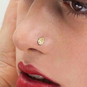Dainty Gold Nose Stud: A close-up of a woman's face, with her eyes closed and her hands covering her ears. She has red lipstick and a nose stud.
