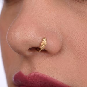 A close-up of a person's nose with a gold-colored nose ring featuring a leaf design.