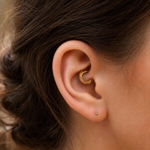 A close-up view of a person's ear with a gold earring in the earlobe.