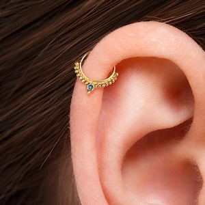 A gold earring with a blue gemstone is visible in the image.