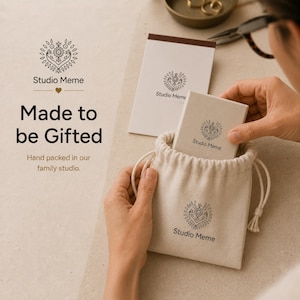 A person is holding a small white bag with the Studio Meme logo, and there is a small white box with the Studio Meme logo inside it. The text above the image reads "Made to be Gifted Hand packed in our family studio."