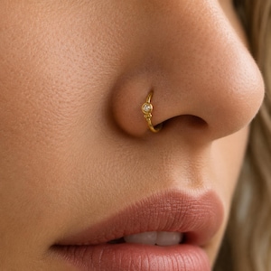 A close-up of a person's nose and lips, with a gold nose ring featuring a small diamond accent.