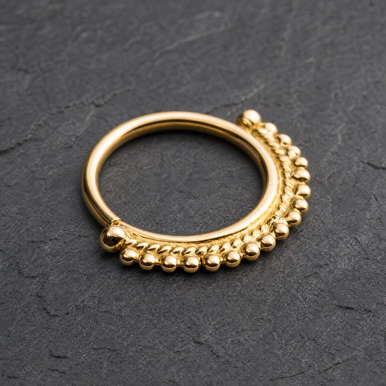 A gold-colored ring with a decorative bezel is displayed on a dark surface.