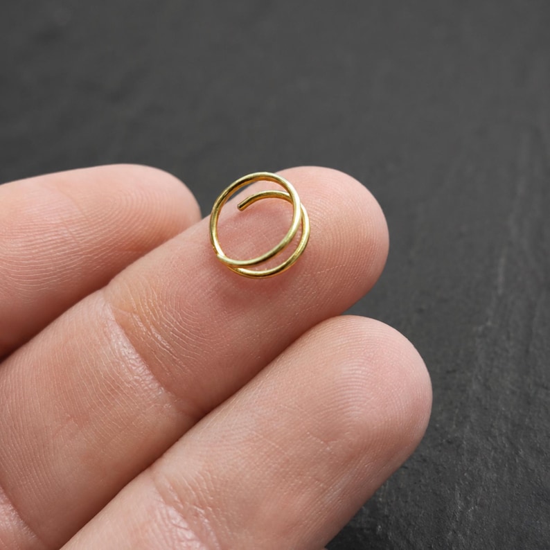 A gold-colored ring is being held in a person's hand against a dark background.