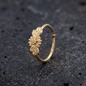 A gold-colored ring with a floral design on a dark surface.