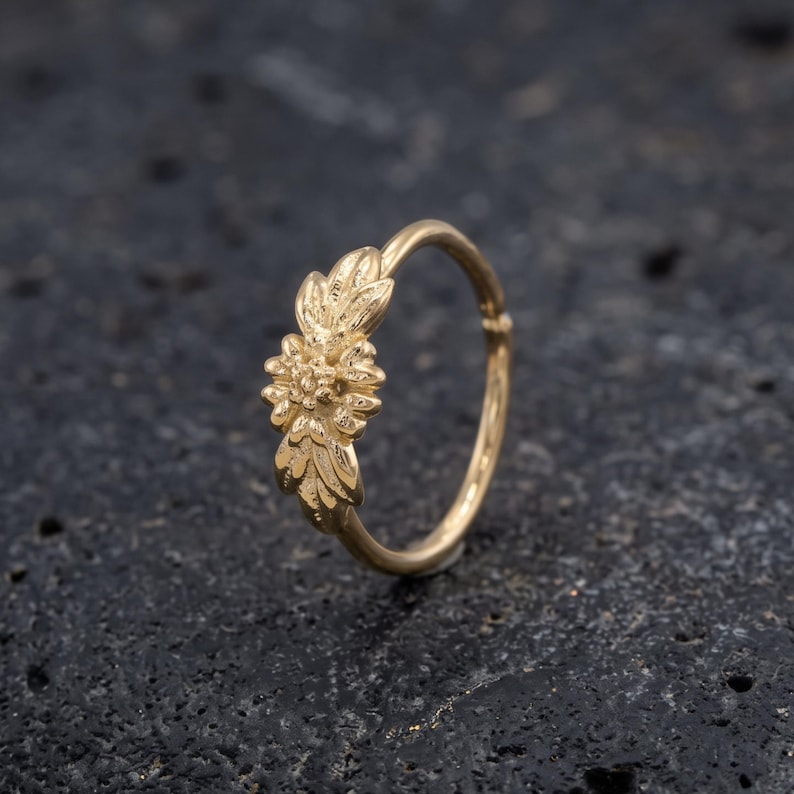 A gold-colored ring with a floral design on a dark surface.