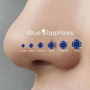 May include: An image displays a series of blue sapphire nose studs in varying sizes, ranging from 1.5mm to 4mm. The text "Blue Sapphires" is above the studs. Each stud has a gold setting, showcasing the deep blue gemstones.