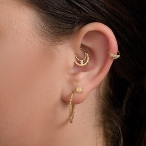 A close-up of a person's ear adorned with multiple gold earrings, including a hoop earring, a stud earring, and a ring earring.
