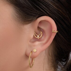 A close-up of a person's ear adorned with multiple gold earrings, including hoop earrings and a piercing.