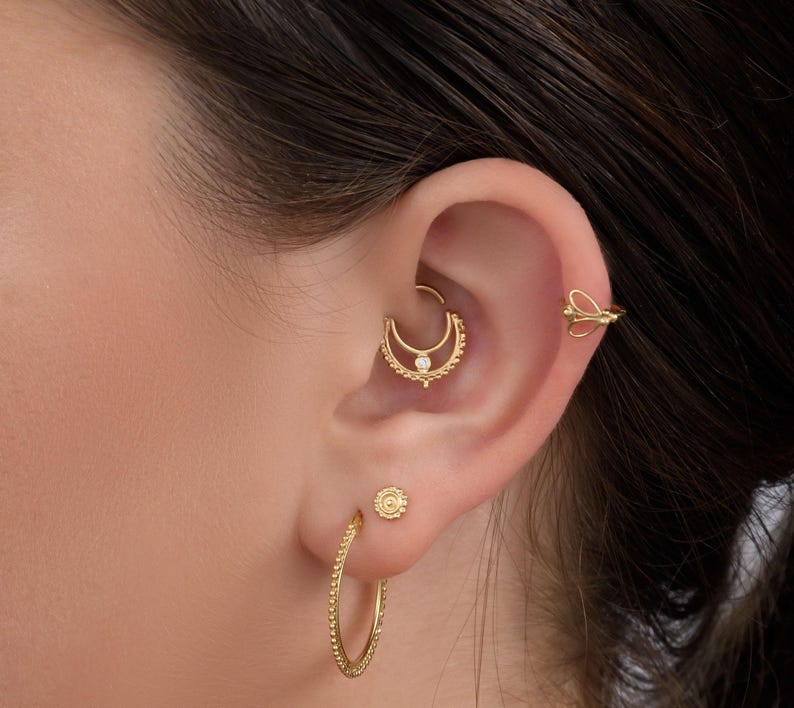 A close-up of a person's ear adorned with multiple gold earrings, including hoop earrings and a piercing.