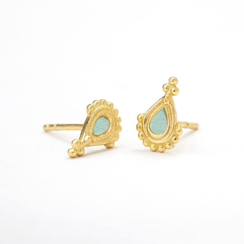 a pair of gold earrings with teal-colored stones, placed side by side on a white background.