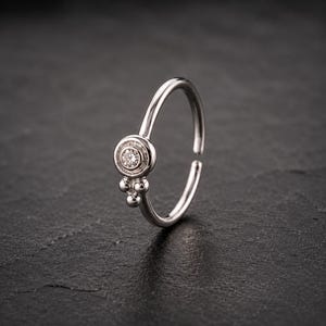 A silver ring with a small diamond in the center is displayed against a dark background.