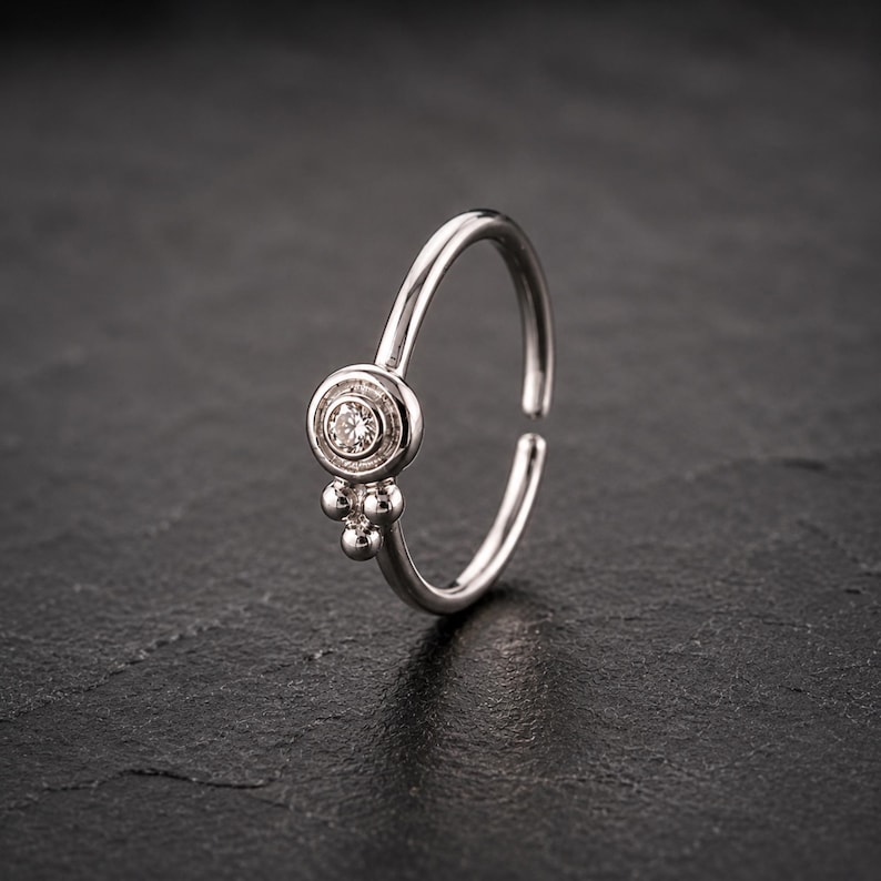 A silver ring with a small diamond in the center is displayed against a dark background.