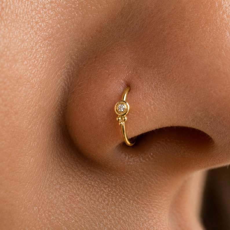 A close-up of a person's nose with a small gold nose ring featuring a diamond.