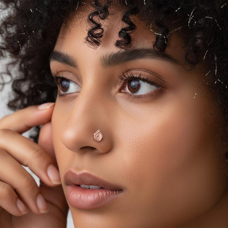 Dainty Rose Gold Nose Stud: A close-up of a woman's face, with her eyes closed and her hands covering her ears. She has red lipstick and a nose stud