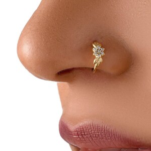 A close-up of a person's nose with a gold-colored nose ring featuring a small flower-like design.