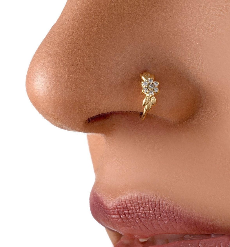 A close-up of a person's nose with a gold-colored nose ring featuring a small flower-like design.