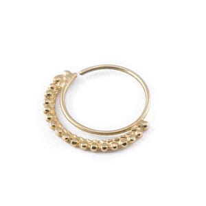 A gold-colored ring with a curved band and a row of small, round beads or stones attached to it.