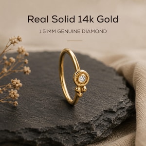 a gold ring with a diamond set in the center, placed on a black rock.