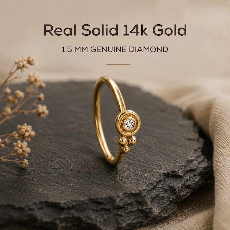 a gold ring with a diamond set in the center, placed on a black rock.