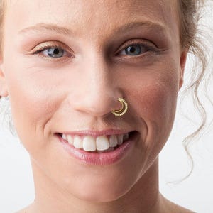 A close-up portrait of a smiling woman with a nose ring, her eyes looking directly at the camera.