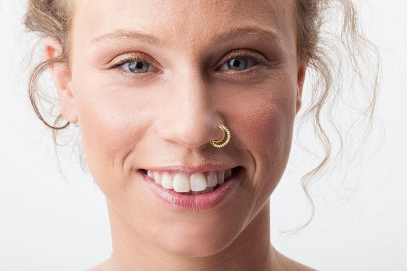 A close-up portrait of a smiling woman with a nose ring, her eyes looking directly at the camera.