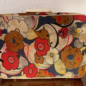 Peut inclure: Une valise vintage avec un motif floral dans des tons de rouge, marron, blanc et bleu. La valise a une poignée blanche et une bordure blanche autour des bords.
