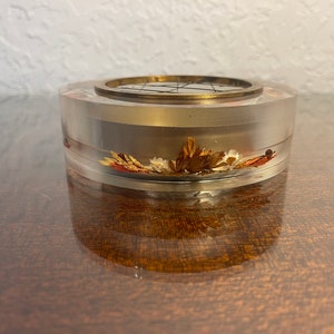 May include: A clear acrylic round container with a brass top and dried flowers inside.
