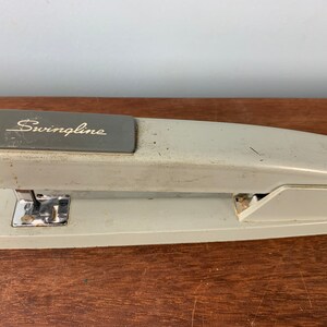 May include: A gray Swingline stapler with a silver staple remover. The stapler is on a wooden surface.