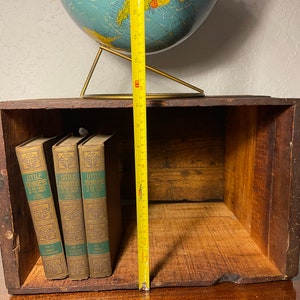 Może przedstawiać: Drewniana skrzynia z trzema książkami zatytułowanymi "Little Journeys to the Homes of Great Musicians" w środku. Skrzynia ma 30,5 cm wysokości i ma na górze globus.
