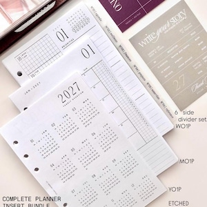 May include: A complete planner insert bundle featuring A5 size white paper sheets with black ink. The set includes a 2027 yearly overview calendar, daily agenda pages with priority sections, and six side dividers labeled agenda, wellness, finances, projects, notes, and reference.