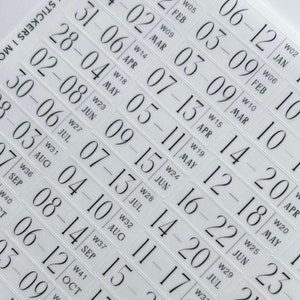 May include: A sheet of white stickers with black numbers and text. The stickers are for a weekly planner and include the days of the week and the week number. The stickers are numbered from 1 to 52, representing the weeks of the year.