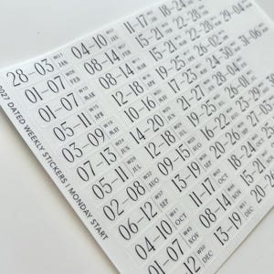 May include: A sheet of clear adhesive stickers featuring black text for 2027 dated weekly planners with a Monday start. The stickers display numerical date ranges for each week of the year, organized by month, with week numbers and month abbreviations.